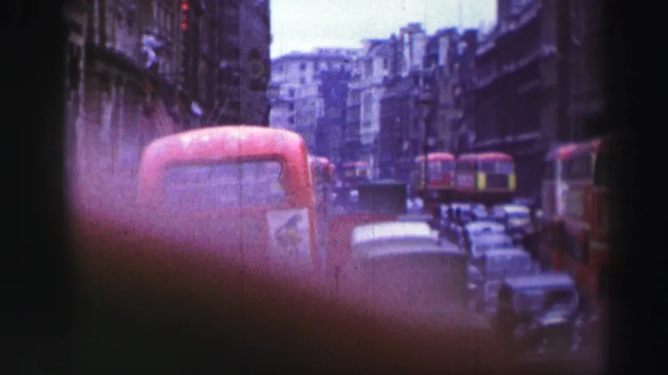 1952 city-traffic frame with red buses, vintage automobiles, stone buildings, and soft handheld 8mm framing.