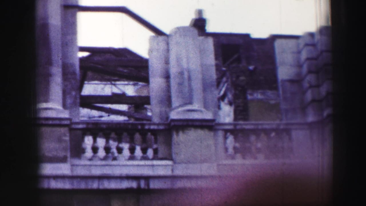 Stone building facade with balcony balustrade, columns, and damaged upper roofline.
