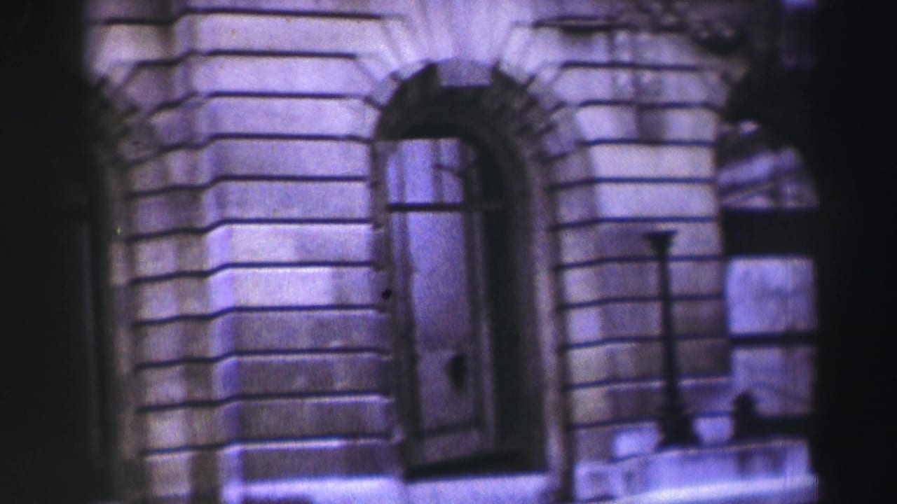 A handheld 8mm view of a grand stone building facade with arched windows and a dark foreground band partly obscuring the center.
