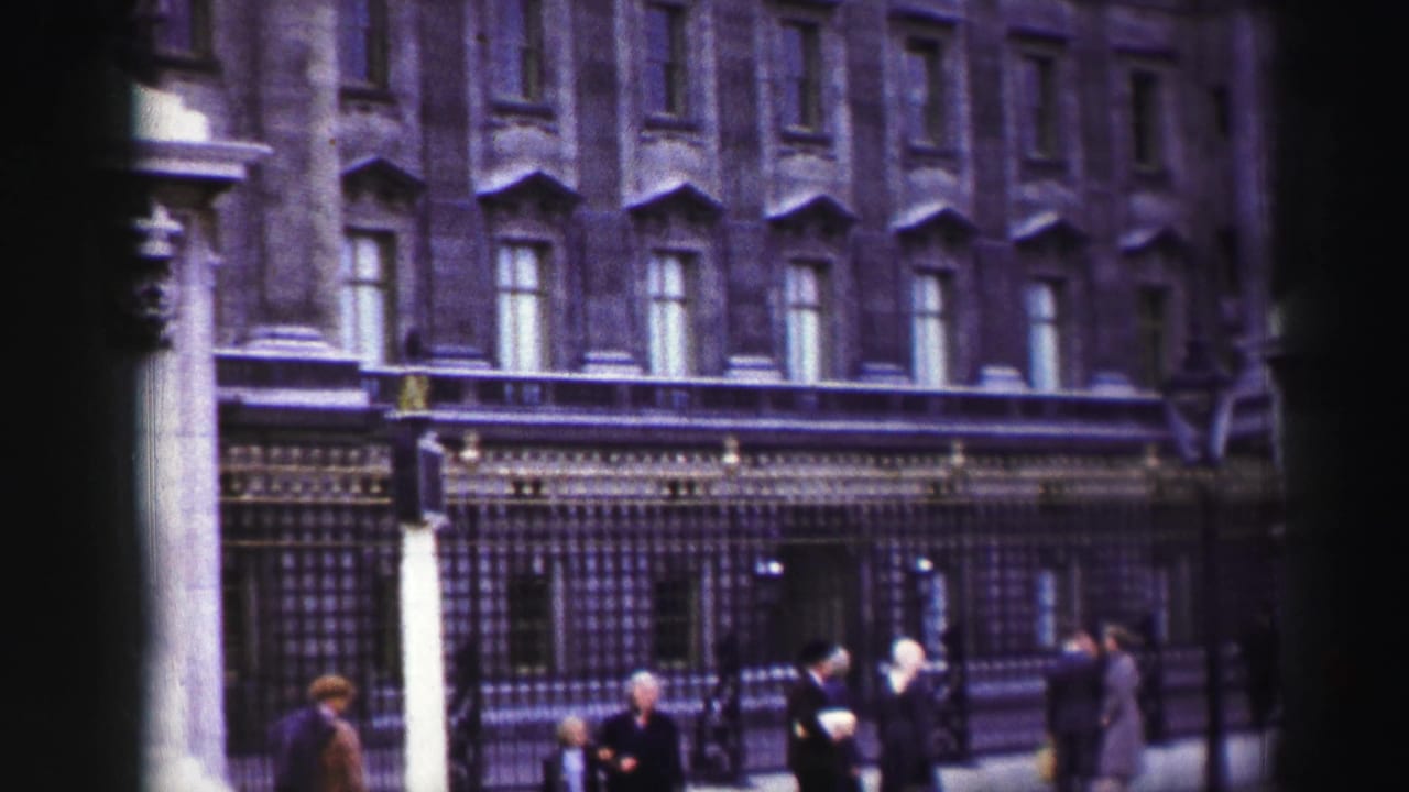 Pedestrians walking beside iron railings in front of a large stone building.