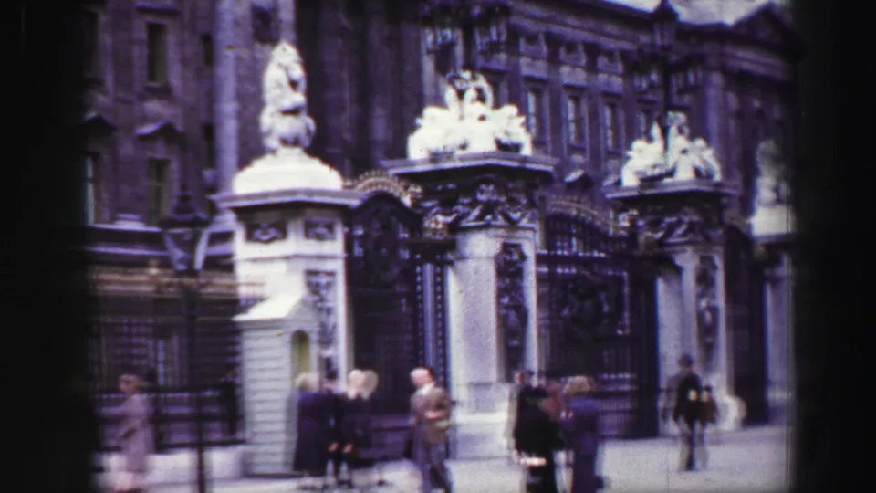 Reported 1952 Scotland home-movie frame showing an ornate gate, stone pillars, statues, and pedestrians near the entrance.