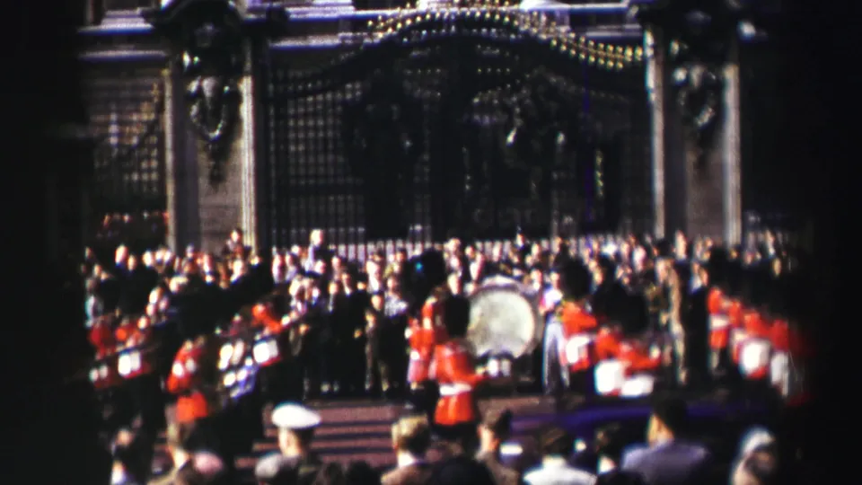 Reported 1952 Scotland frame of guards and drummers moving past a dense crowd in front of an ornate iron gate.