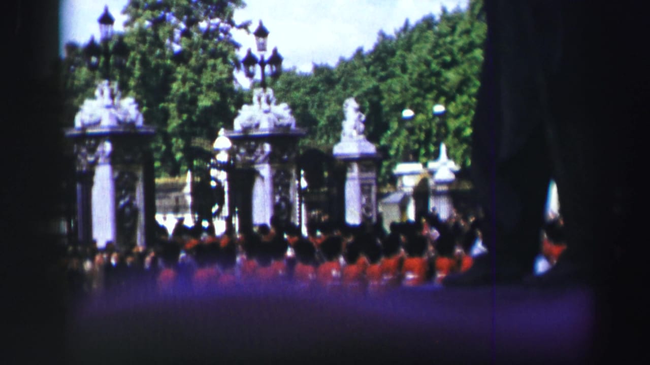 1952 Edinburgh home-movie frame showing red-uniformed soldiers before ornate gates, with spectators in the foreground and trees beyond.