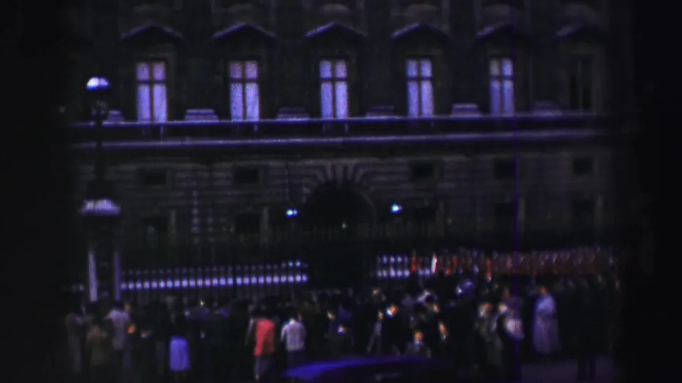 1952 Edinburgh home-movie view of a large historic facade with railings, spectators, and red-uniformed soldiers along the street.