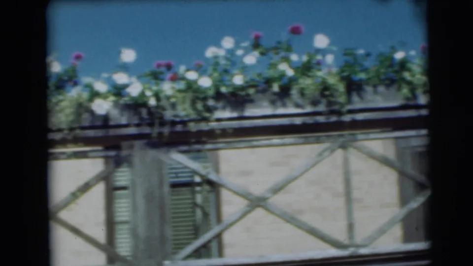 1954 Pennington, New Jersey home-movie frame showing a balcony flower box above a pale facade and X-braced railing.