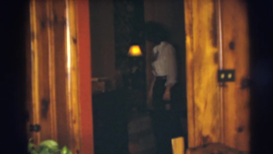 A 1954 Pennington home-movie frame shows the woman leaning or walking forward in a dim interior with warm wood trim.