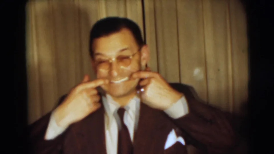 The suited man in the 1954 Pennington interior playfully pulls his mouth into a smile for the home-movie camera.