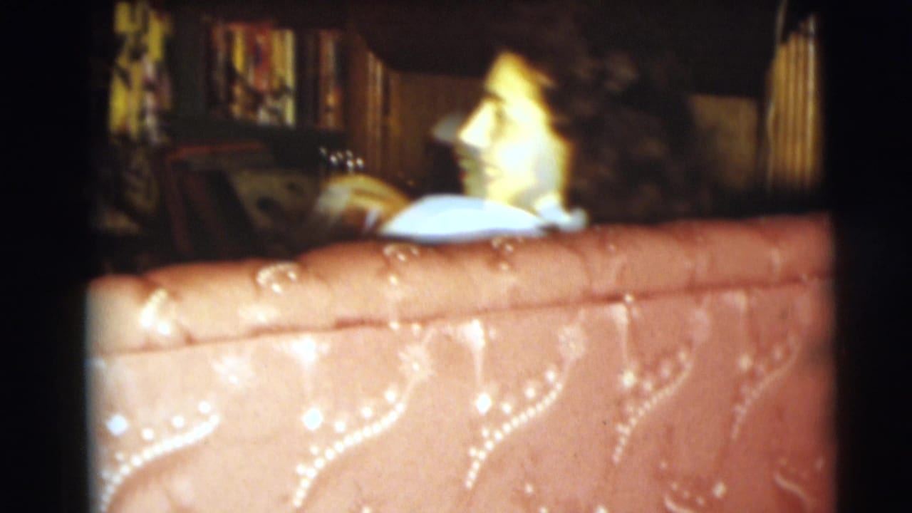 Woman seated behind a red tufted sofa in a dim living room.