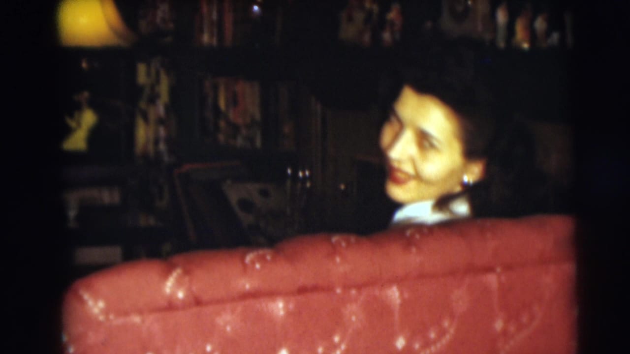 Woman smiling behind a red tufted sofa in a dim living room.