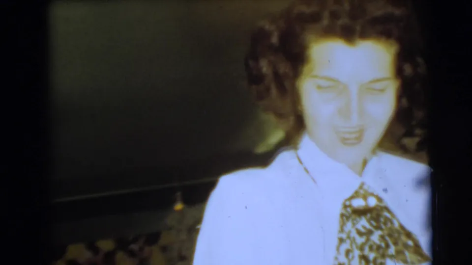 A woman in a white blouse and patterned tie or scarf faces the camera in this soft 1954 Pennington home-movie frame.