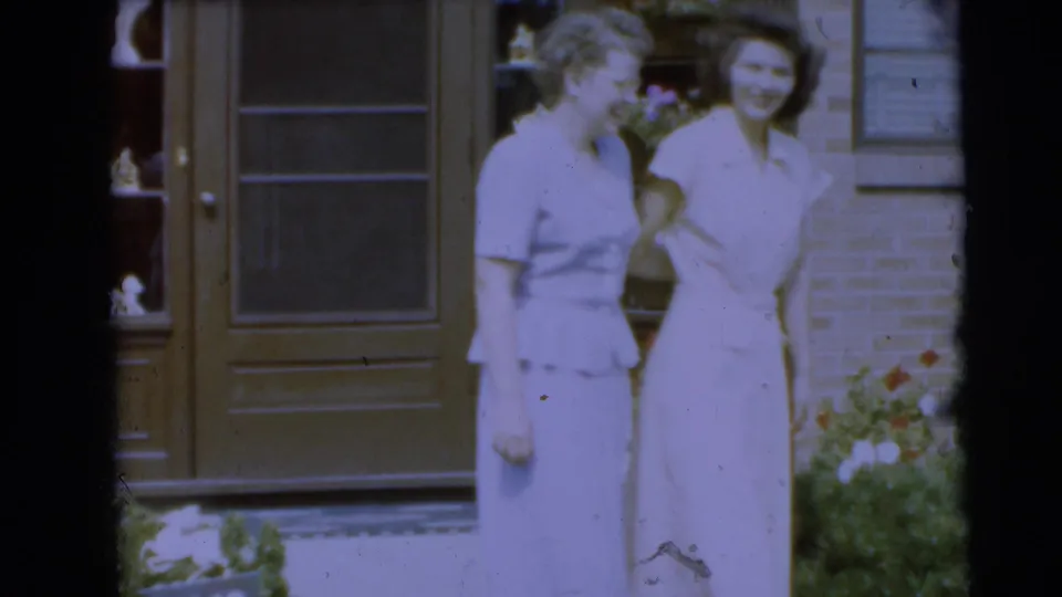 Two young women in light dresses smile outside a brick house in Pennington, New Jersey, in 1954.
