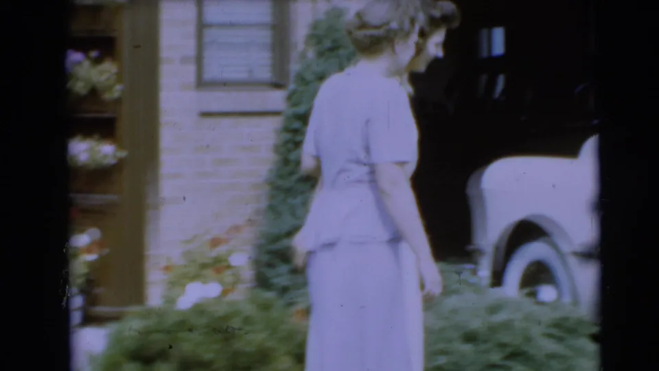 The women walk from the brick house toward a pale convertible in this 1954 Pennington home-movie frame.