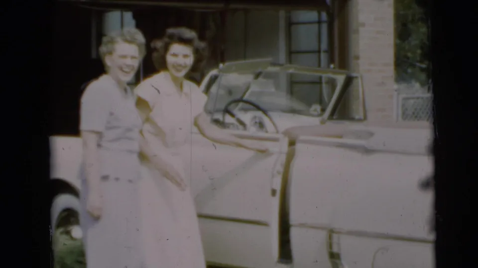 Two young women smile beside a pale convertible outside a Pennington, New Jersey home in 1954.