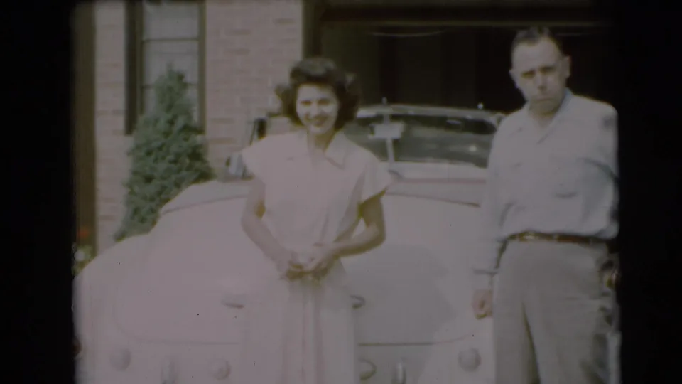 In Pennington, New Jersey, 1954, a young woman and man stand near a pale vintage car in front of a brick residence.
