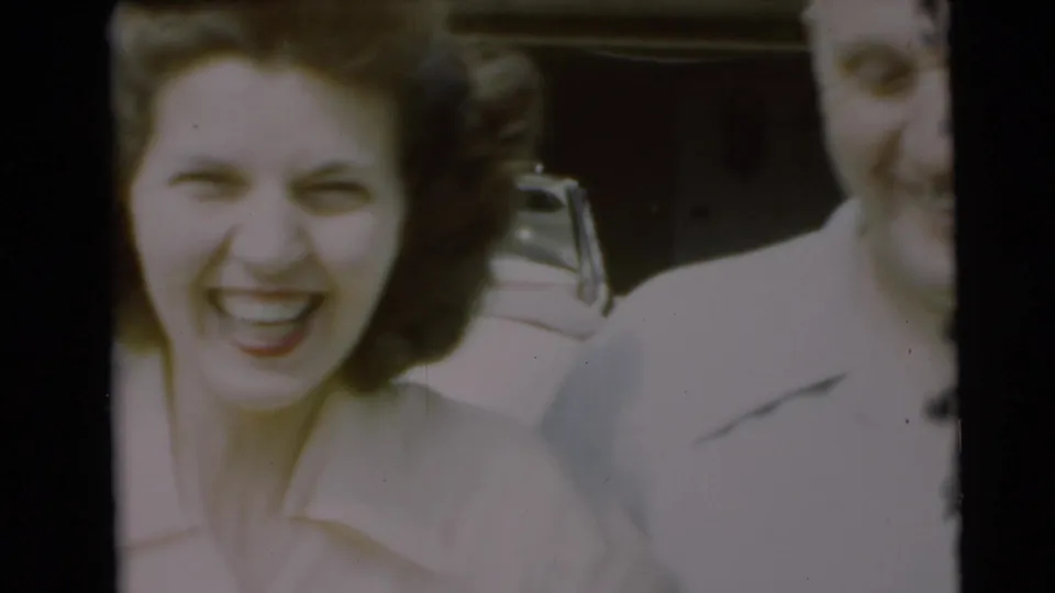 Close framing shows the woman laughing toward the camera, with the man partly cropped and the car behind them.