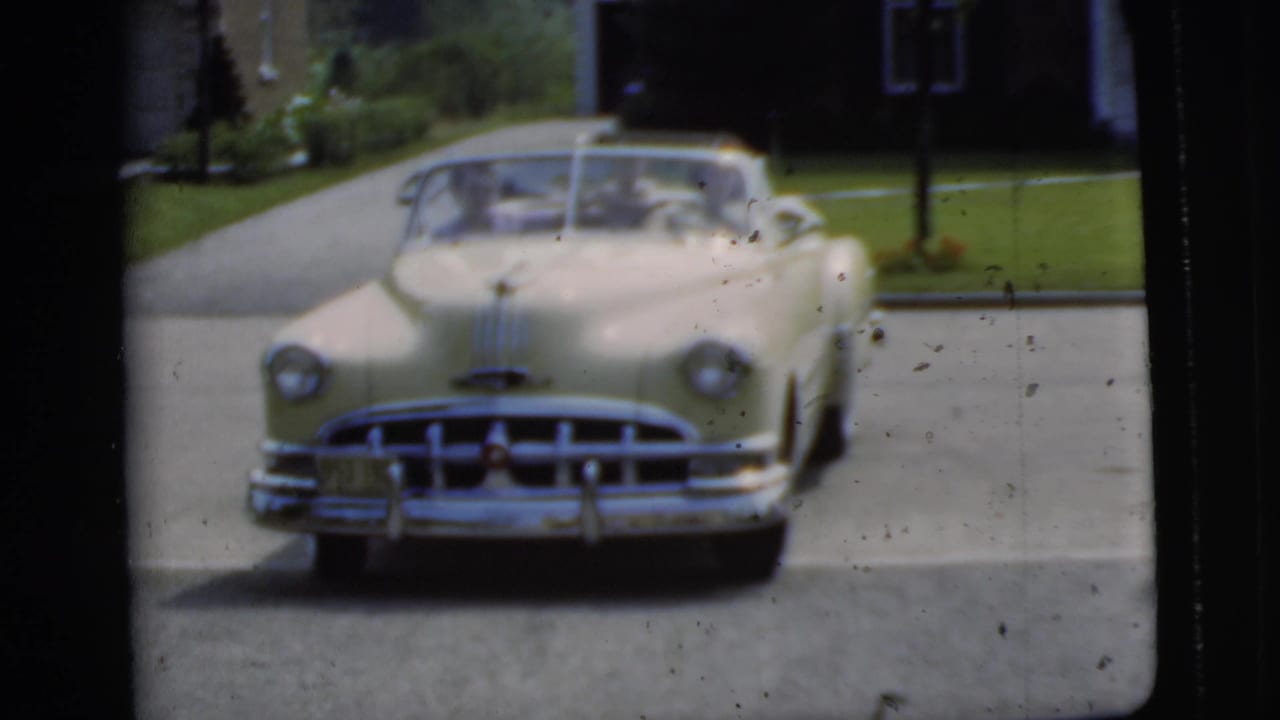 Yellow convertible facing the camera in a suburban driveway.