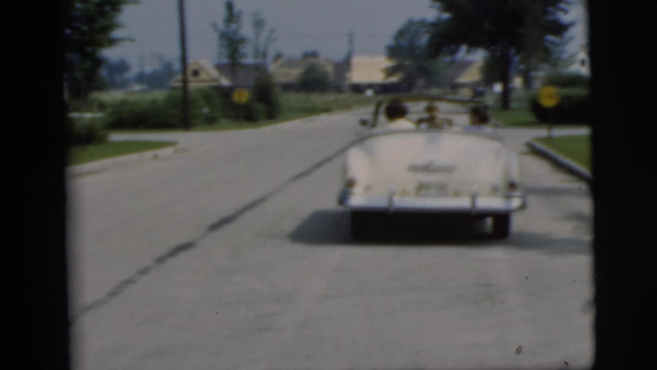 White convertible driving away on a quiet suburban street.