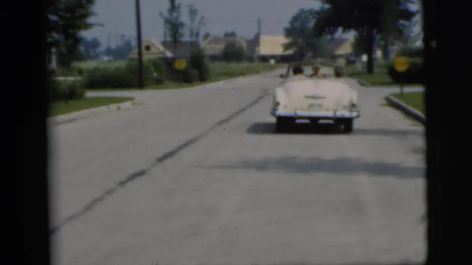 The white convertible continues away on a mid-century suburban road in the Pennington 1955 clip.