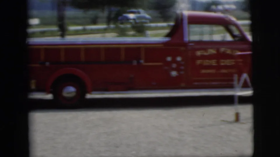 A red fire truck with lettering is parked at an outdoor community setting in the supplied 1955 Pennington footage.