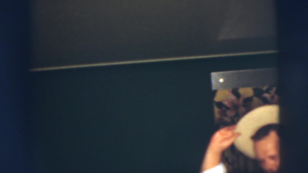 Young man lifts or adjusts a light-colored hat in a dim room.
