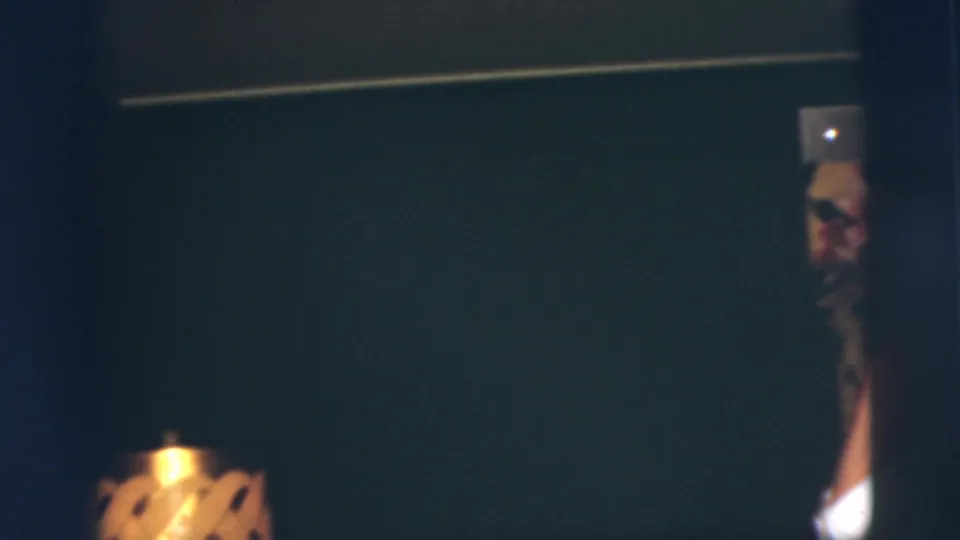 At the edge of the frame, part of the young man and his light hat remain visible against the dark interior wall.