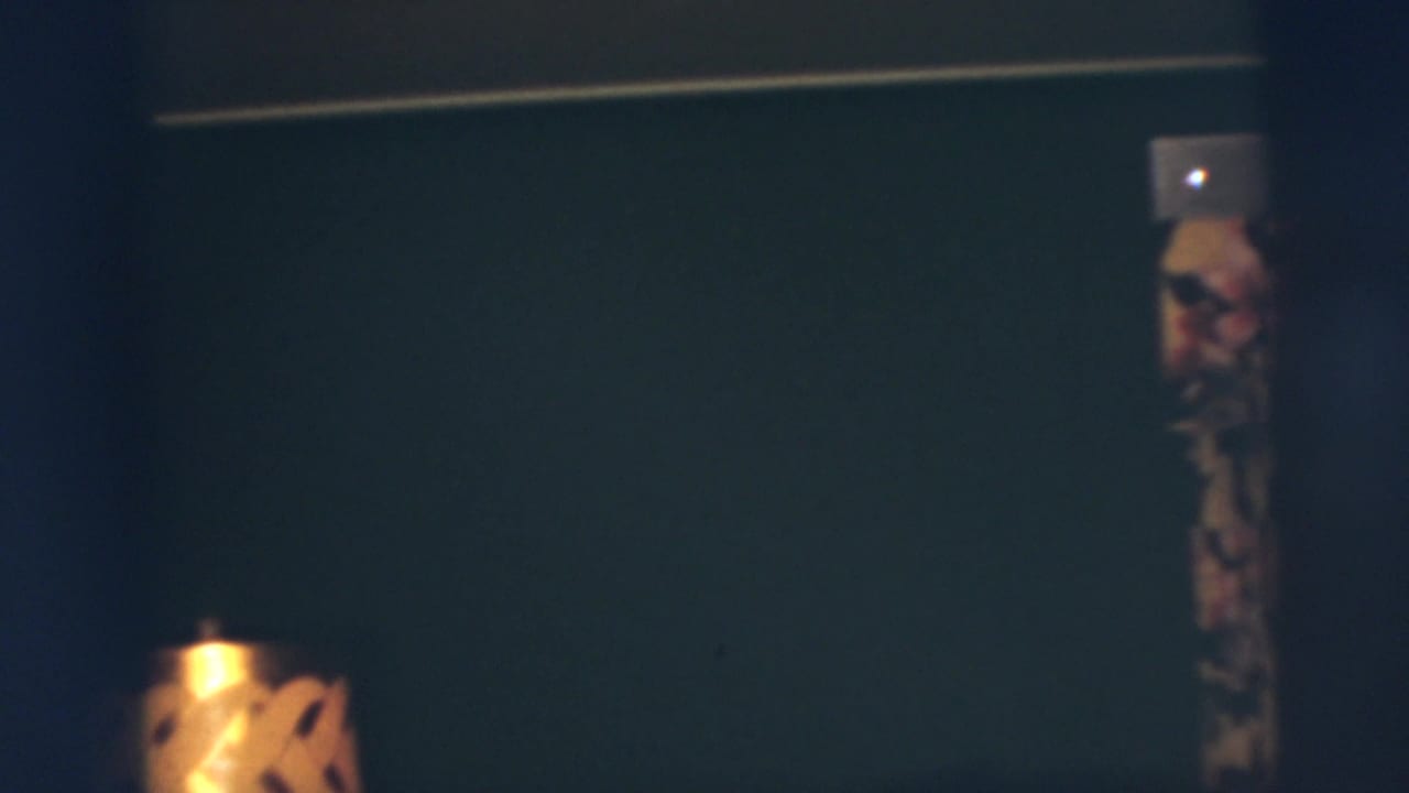 Dim Pennington, New Jersey home-movie interior from 1955 with a dark wall, lamp shade edge and partial adult figure.