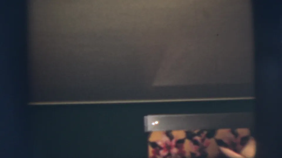 Pennington, New Jersey 1955 home-movie frame showing a dim interior detail with floral patterning and a pale hat-like form near the lower edge.