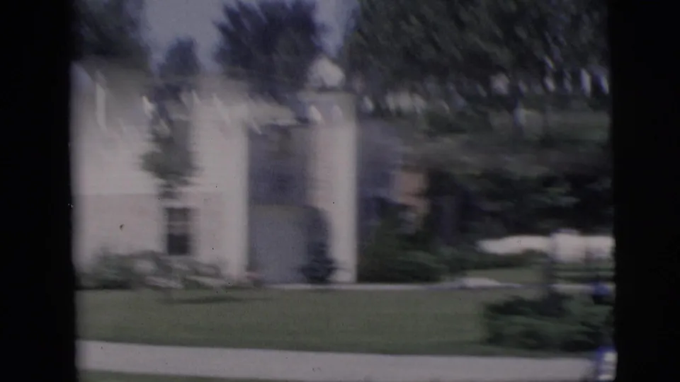Handheld 8mm frame from Pennington showing a motion-blurred residential lawn, trees, and a light-colored house near the street.
