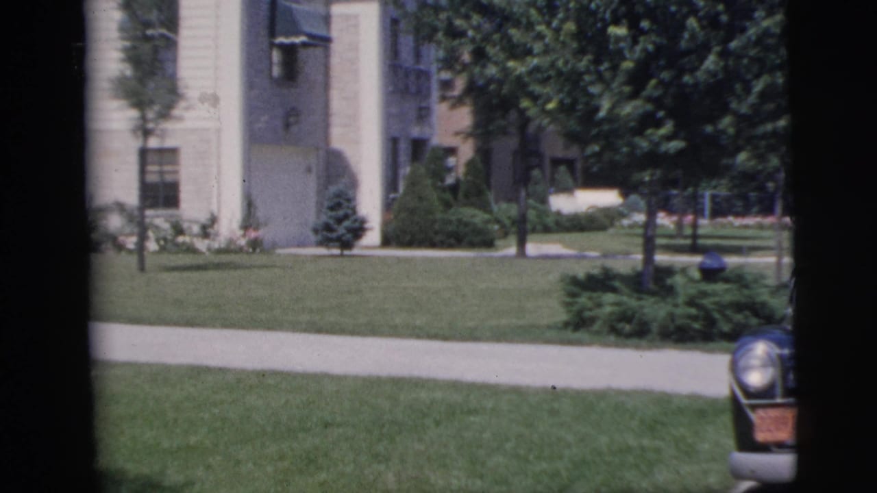1955 Pennington residential scene showing a pale building, entrance area, lawn, trees, sidewalk, and the front edge of a parked car.