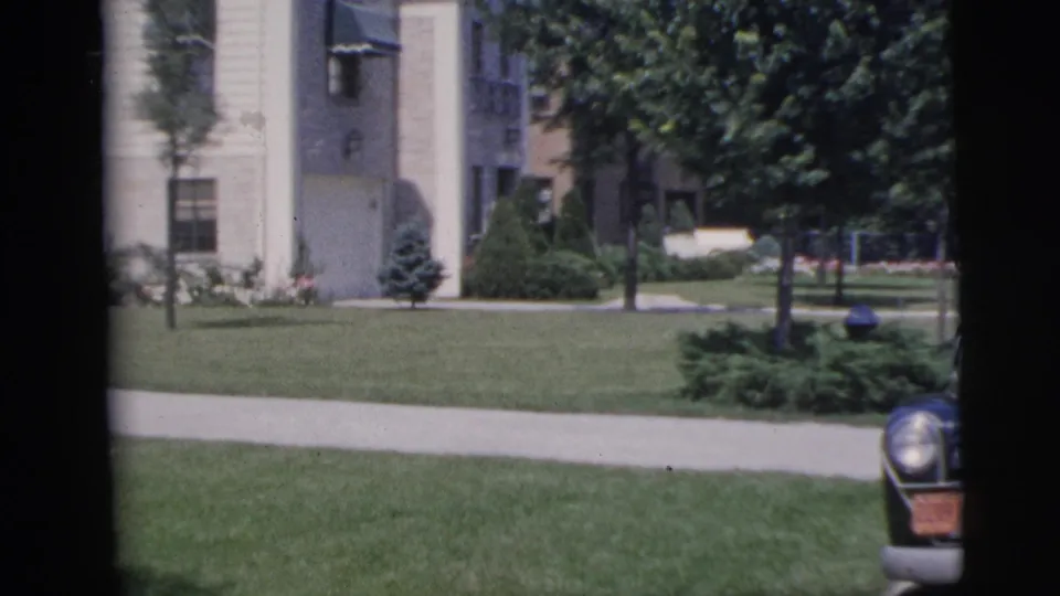 1955 Pennington residential scene showing a pale building, entrance area, lawn, trees, sidewalk, and the front edge of a parked car.
