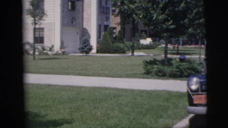 1955 Pennington suburban exterior with a residential building, broad lawn, sidewalk, trees, shrubs, and a partial parked car.