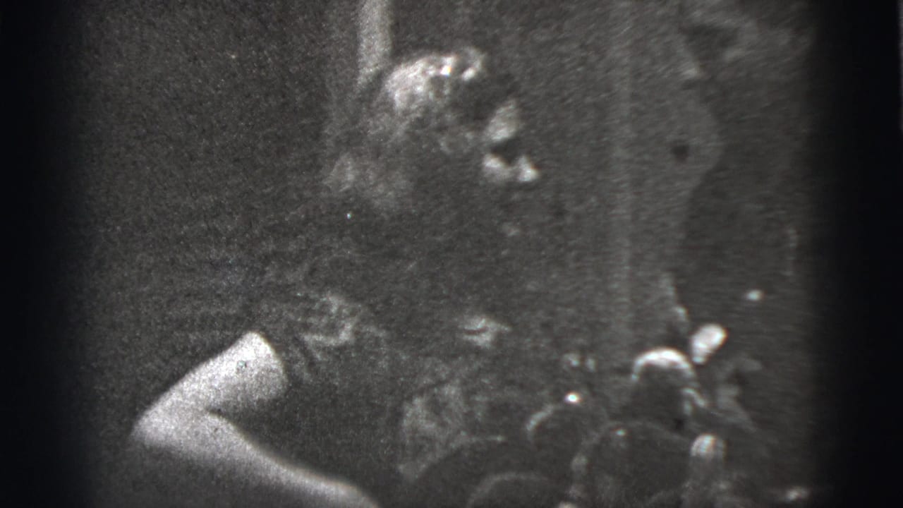 Low-light 1956 New York City 8mm frame showing an adult figure close to the camera amid heavy shadow and grain.