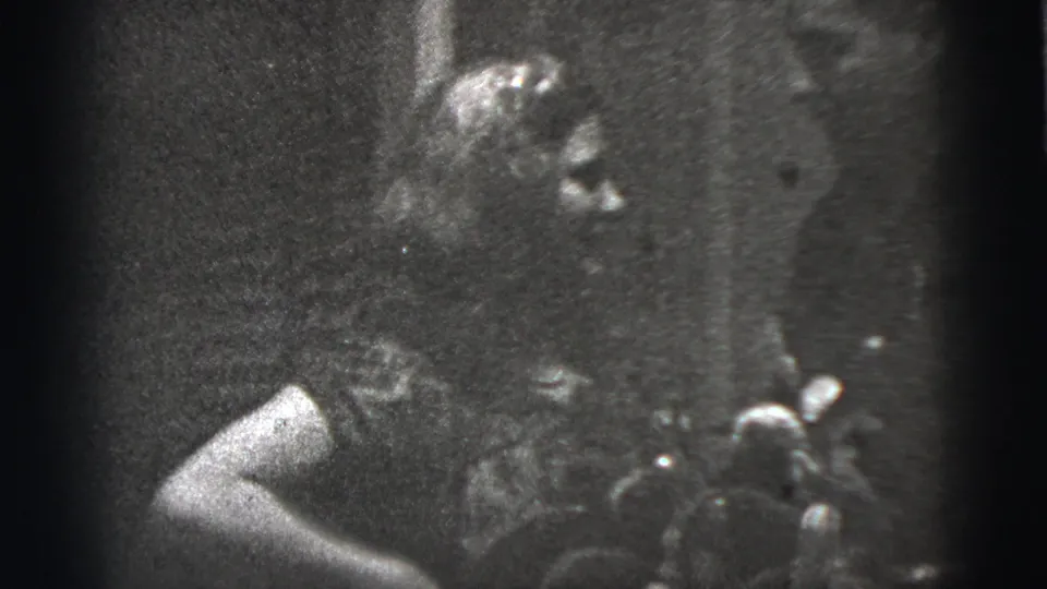 Low-light 1956 New York City 8mm frame showing an adult figure close to the camera amid heavy shadow and grain.