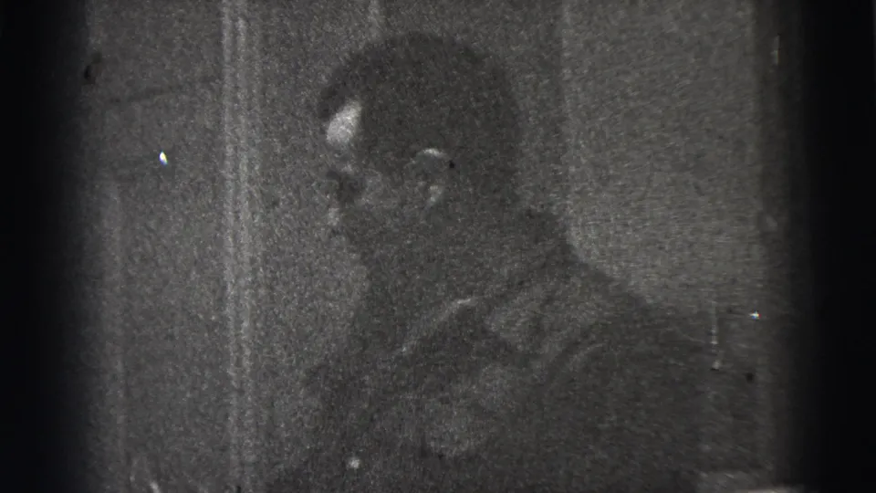 Grainy 1956 New York City home-movie frame of a man in profile, partly hidden by darkness near a wall or doorway.