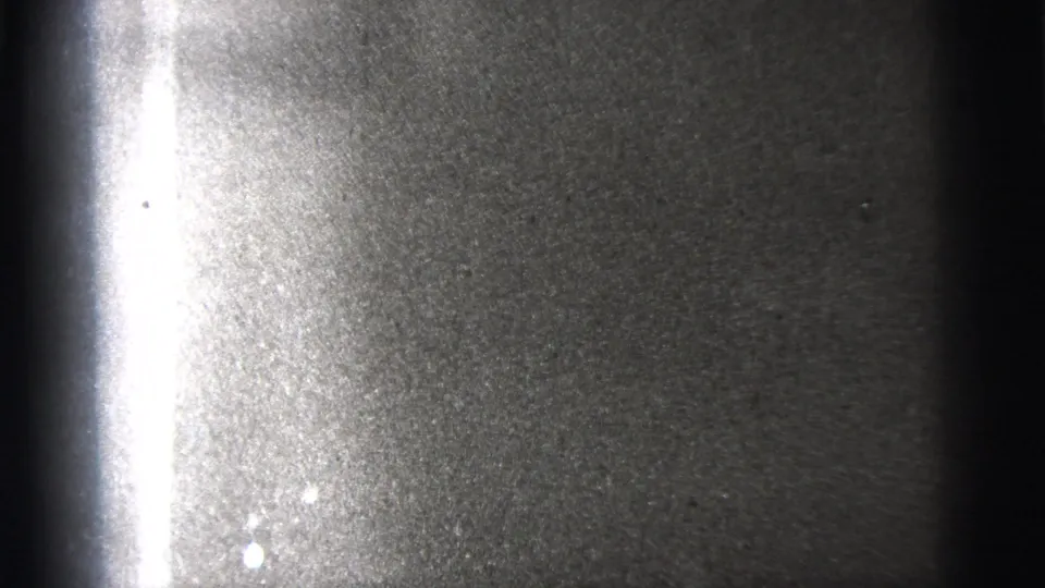 Underexposed 8mm frame from the New York City clip with little visible detail beyond grain and a bright edge flare.