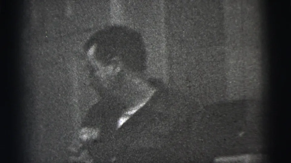 Low-light 1956 New York City 8mm frame showing a man looking downward, his face softened by grain and shadow.