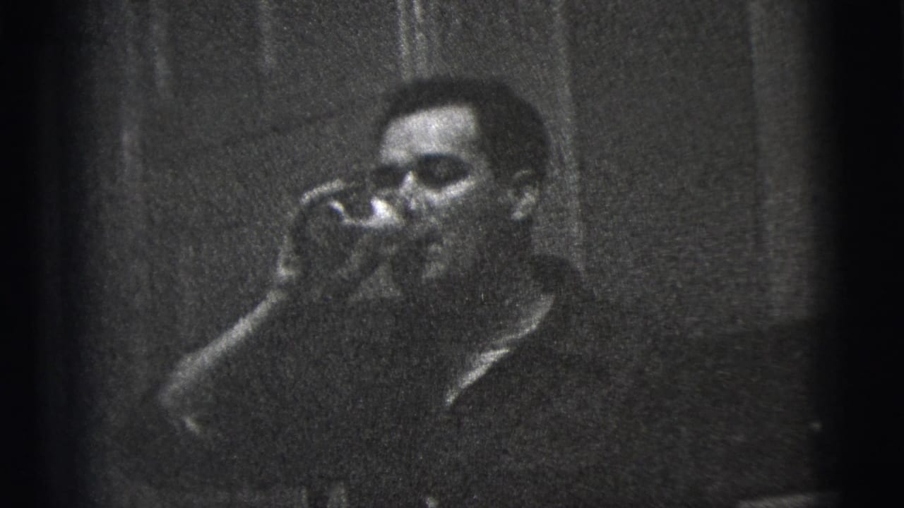 Man in a dark shirt drinks from a glass inside a dim room.