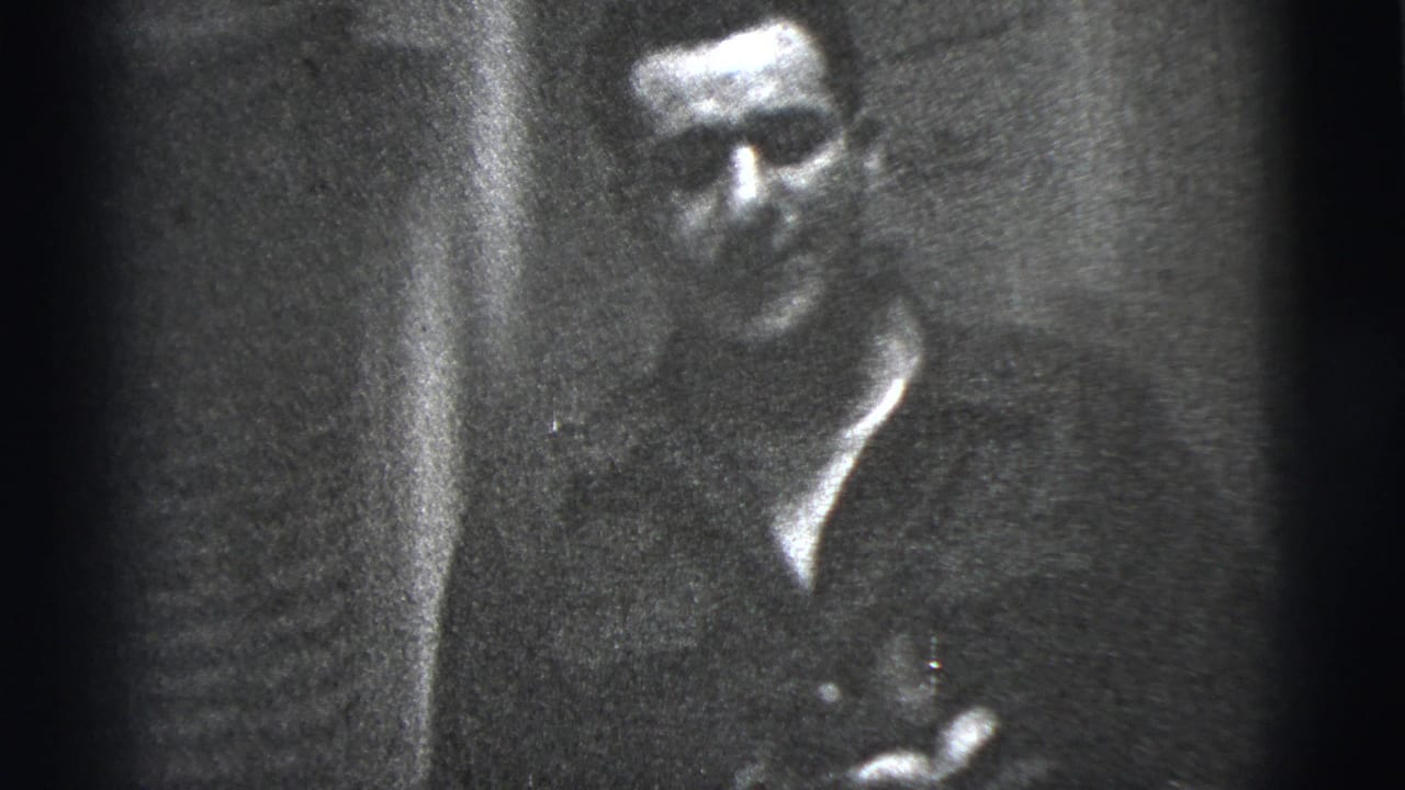 A man sits against a dark interior backdrop in this 1956 New York City 8mm home-movie frame.