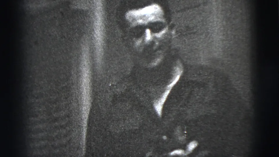 A man sits against a dark interior backdrop in this 1956 New York City 8mm home-movie frame.