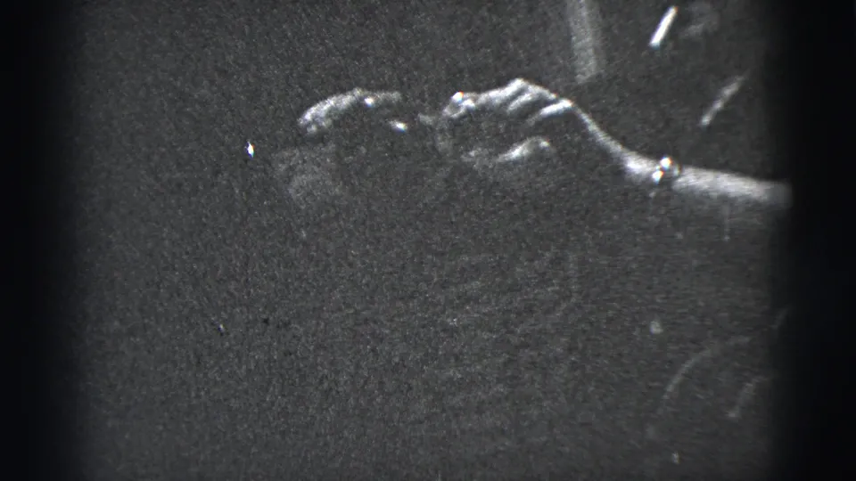 1956 New York City home-movie frame showing a hand, cigarette, bottle, and wristwatch in a dim street close-up.