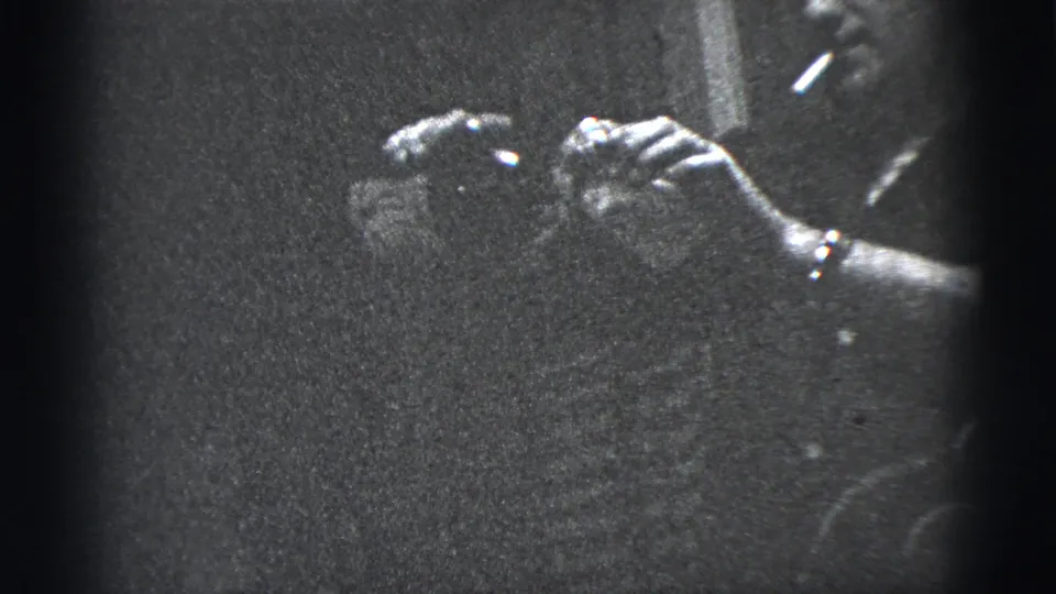 1956 New York City frame showing a cigarette and bottle held close to a dark-clad person, with strong film grain and vignette.