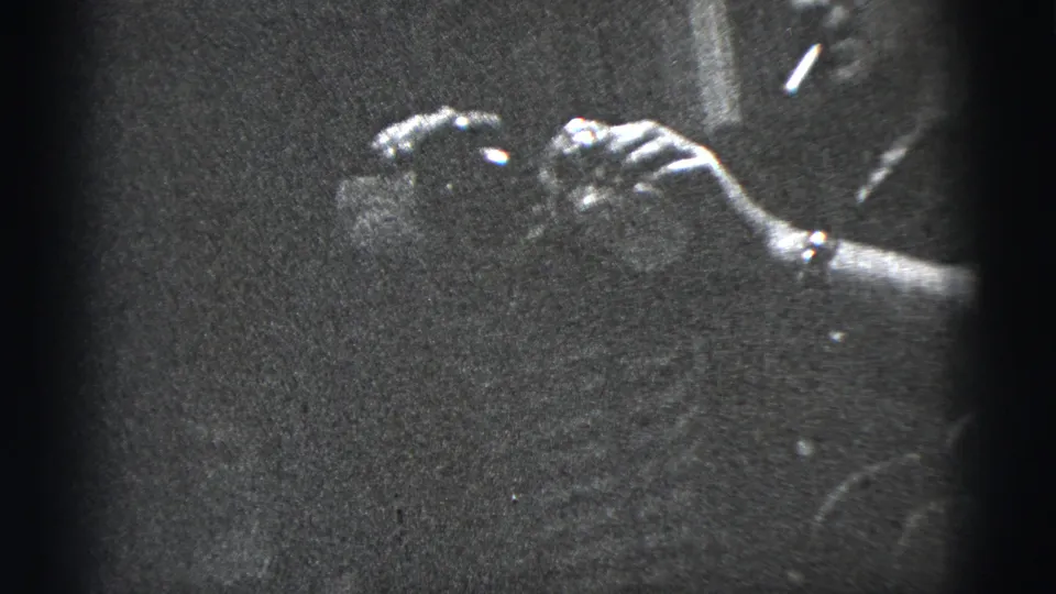 Black-and-white 1956 New York City home-movie frame showing hands with a wristwatch handling a drink in a dark lounge-like interior.