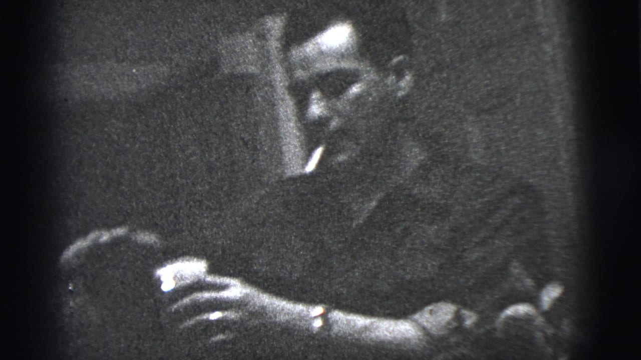 In 1956 New York City home-movie footage, a man and woman stand close together while hands reach toward a small bag or object.