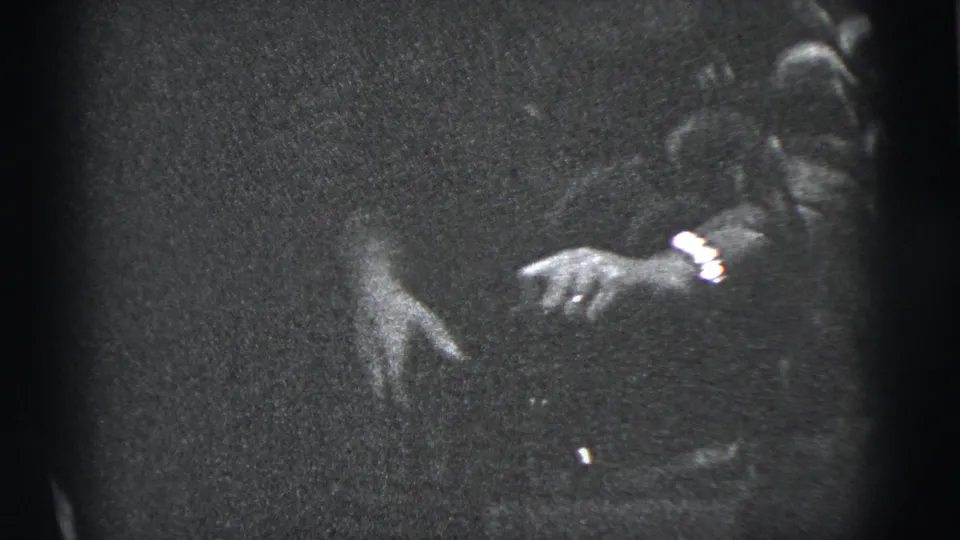 A woman appears at the right side of the frame in 1956 New York City home-movie footage, with her hands visible in low light.