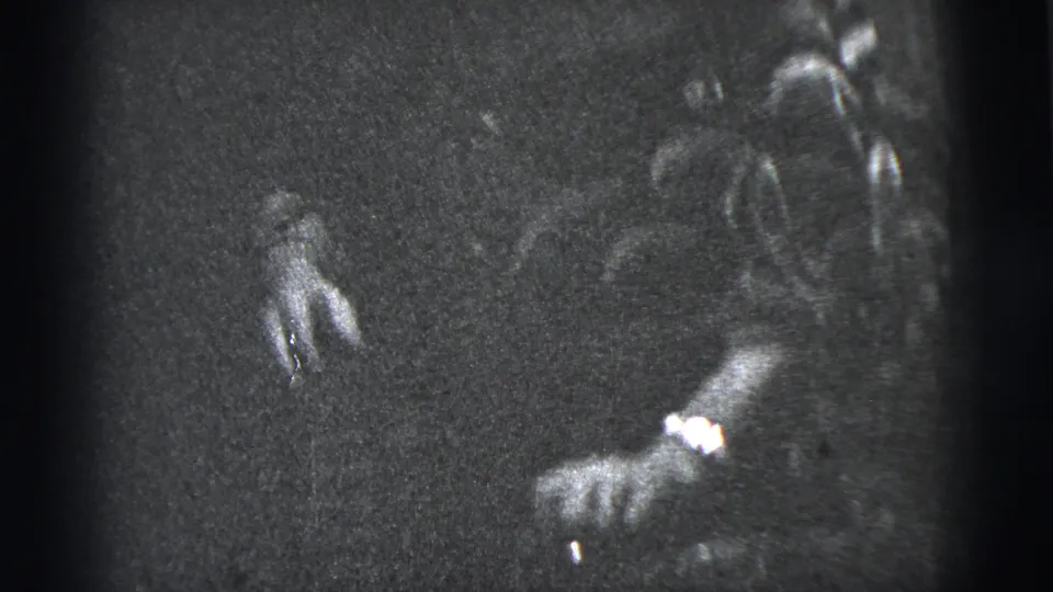 1956 New York City 8mm frame showing indistinct figures near a dark house exterior, with one hand visible at left.