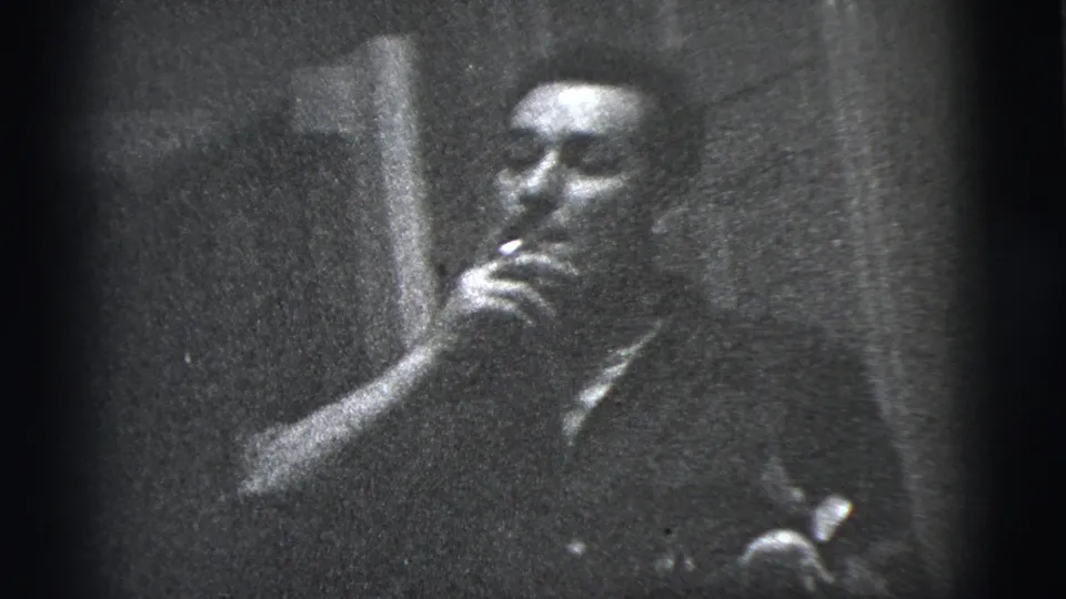 Close 1956 New York City 8mm view of the man smoking beside a wall, with facial features softened by grain and exposure.