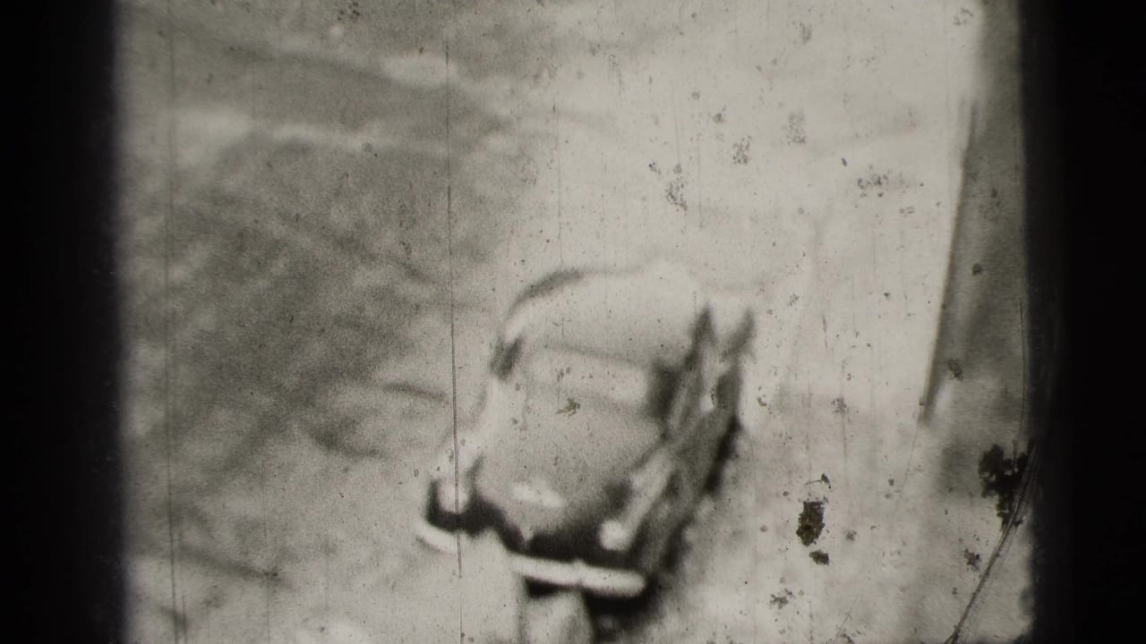 1956 New York City home-movie frame showing a high-angle view of a rounded sedan moving away on a street.