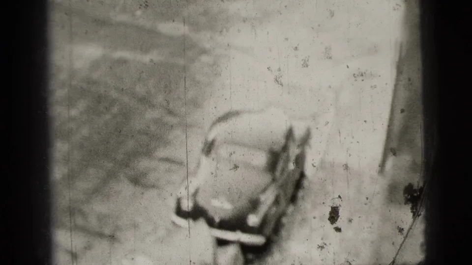 1956 New York City home-movie frame showing a high-angle view of a rounded sedan moving away on a street.