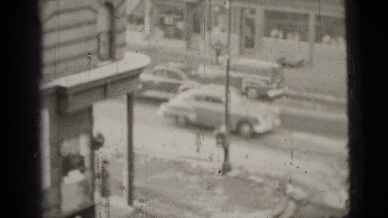 1956 New York City street view with mid-century cars, building facades, and a high-angle home-movie perspective.