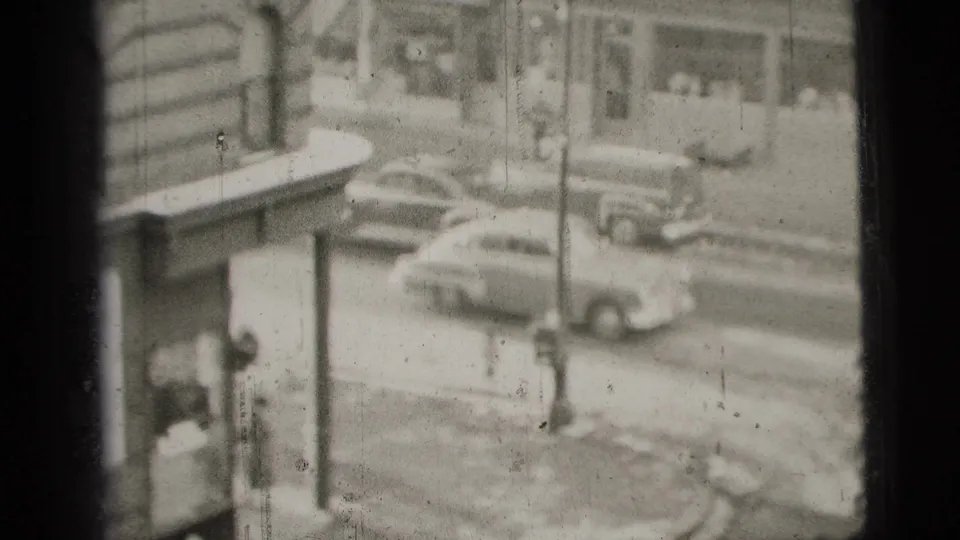 1956 New York City street view with mid-century cars, building facades, and a high-angle home-movie perspective.